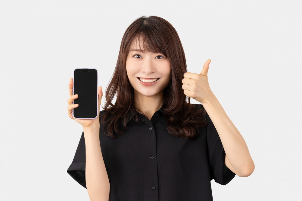 スマホを片手にイイネのポーズをとる女性