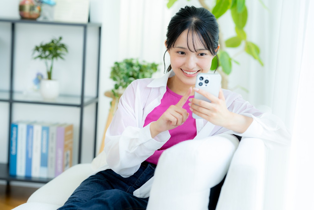 ソファーに腰掛けてスマホで通販を楽しむ女性